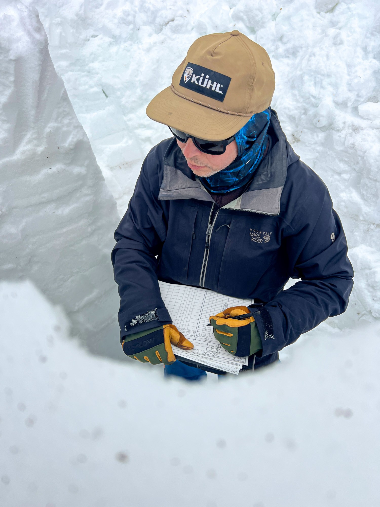 looking down at a researcher standing in a snowy trench with a clipboard of notes