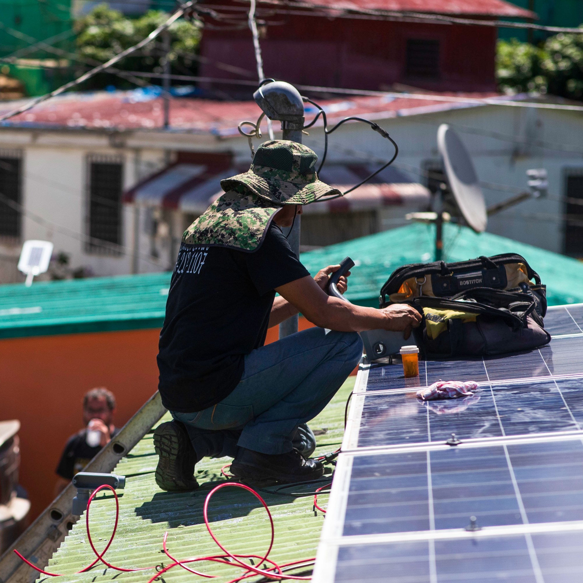 worker crouching on a roof to install solar panels