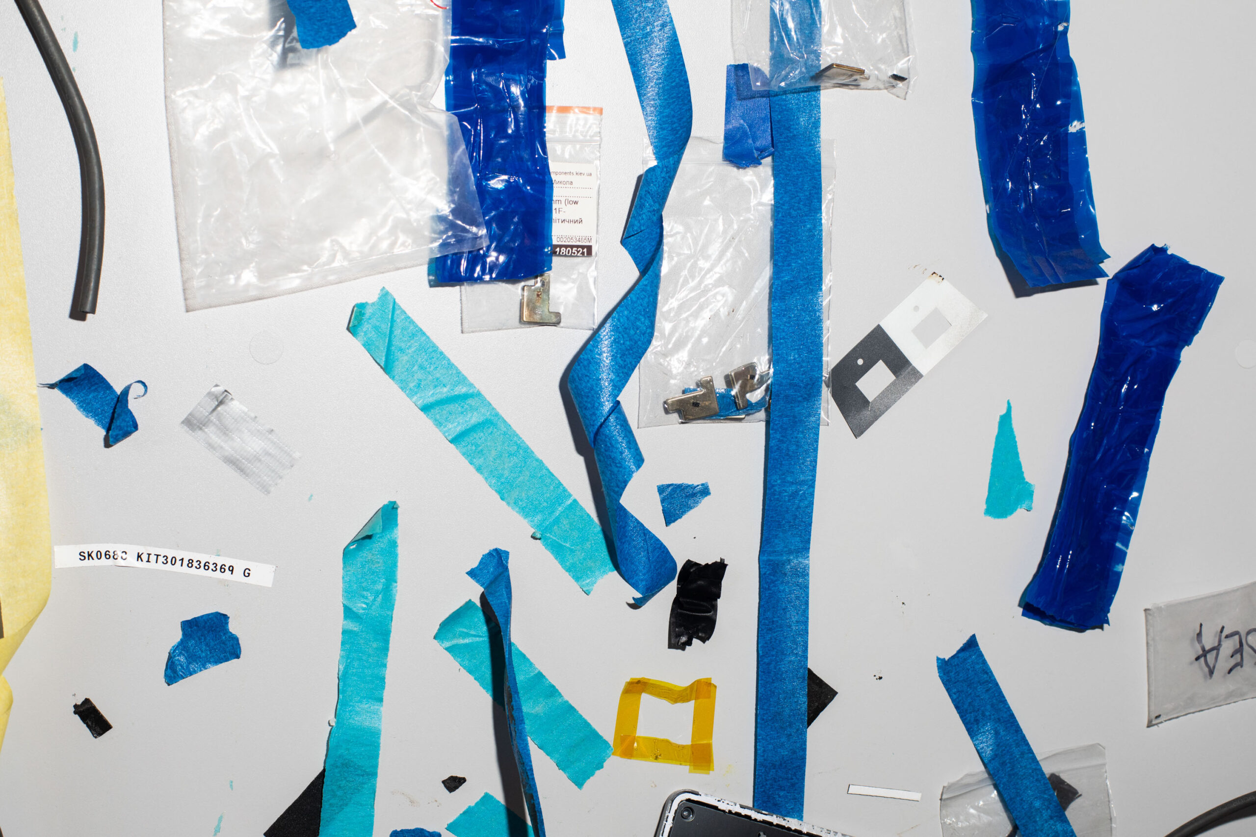 a surface scattered with pieces of used blue tape of various colors and sizes. Two ziploc bags with small metal parts are also taped up.