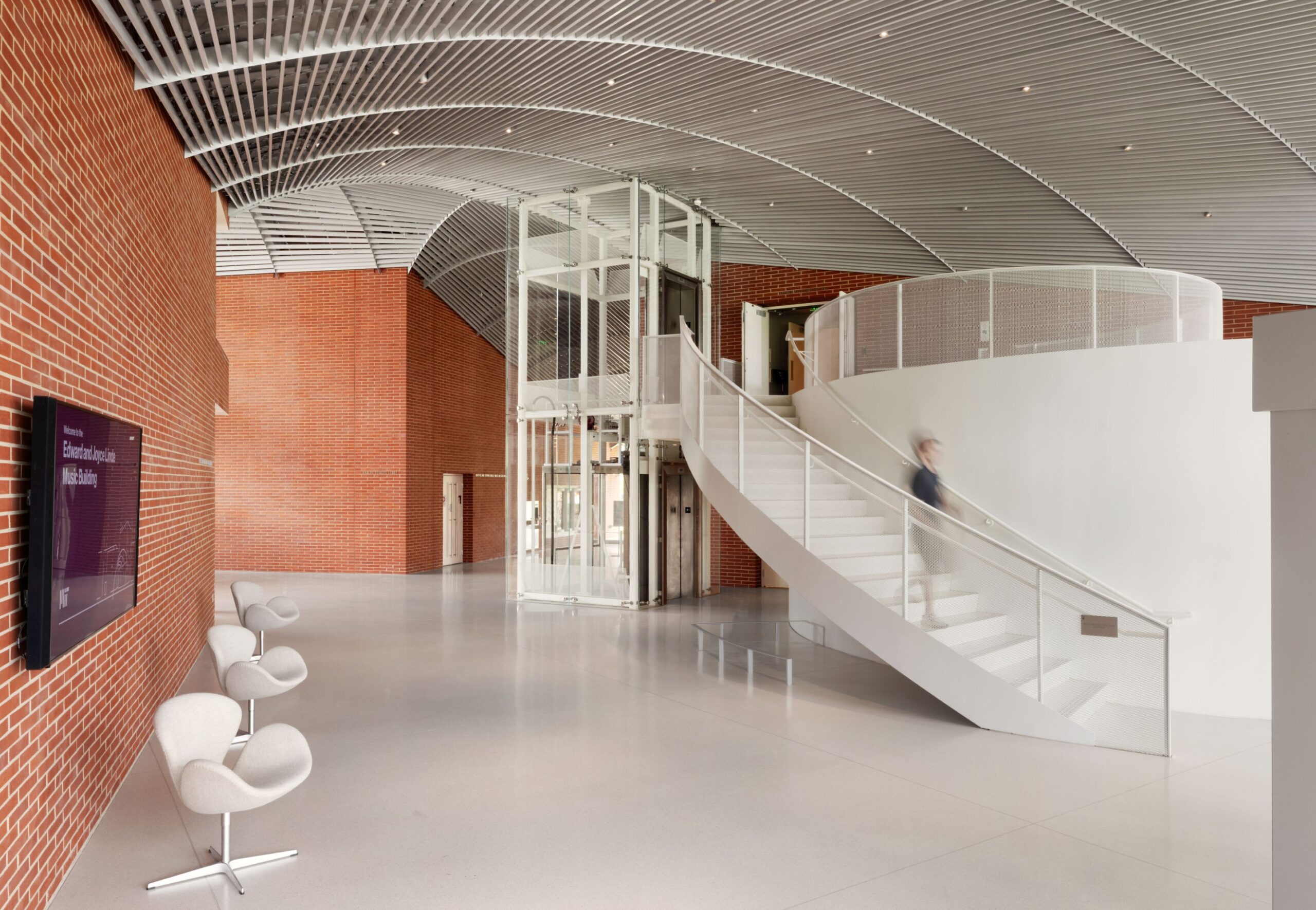 a brick-walled lobby with freestanding elevator next to a white staircase