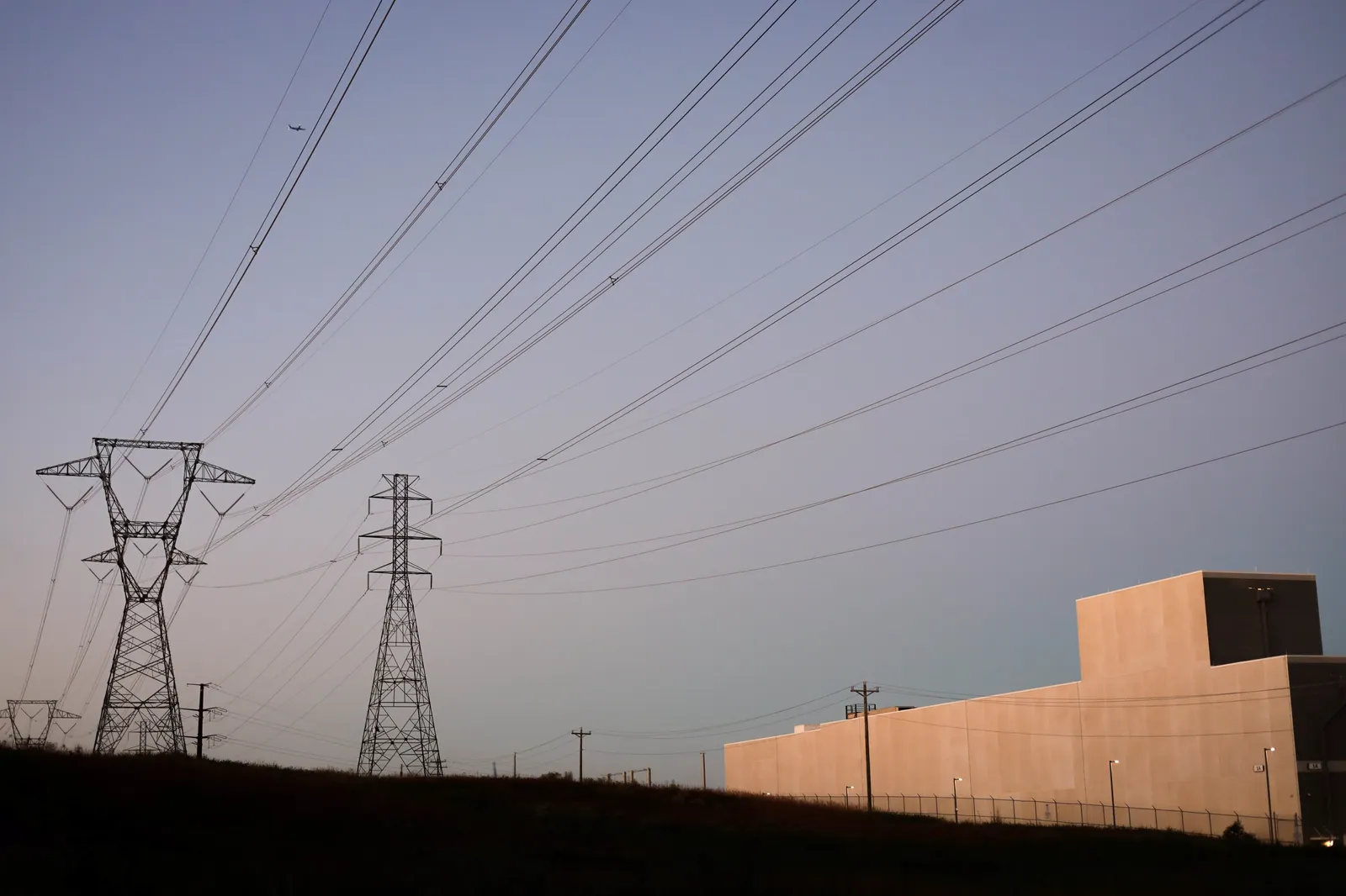 A gray white and data center seen next to power lines against a twilight sky.