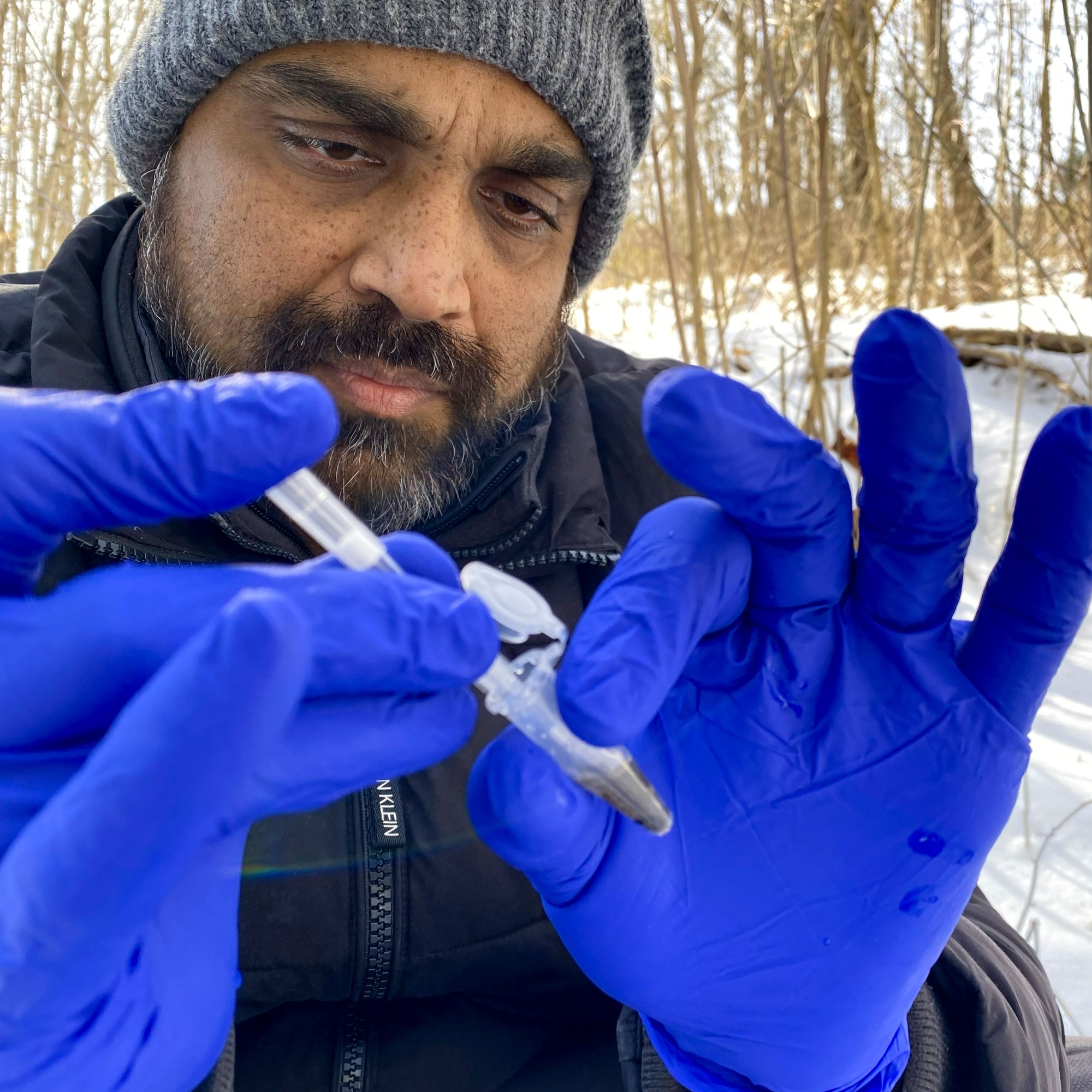 closeup on the gloved hands of a man outside with a DNA test kit