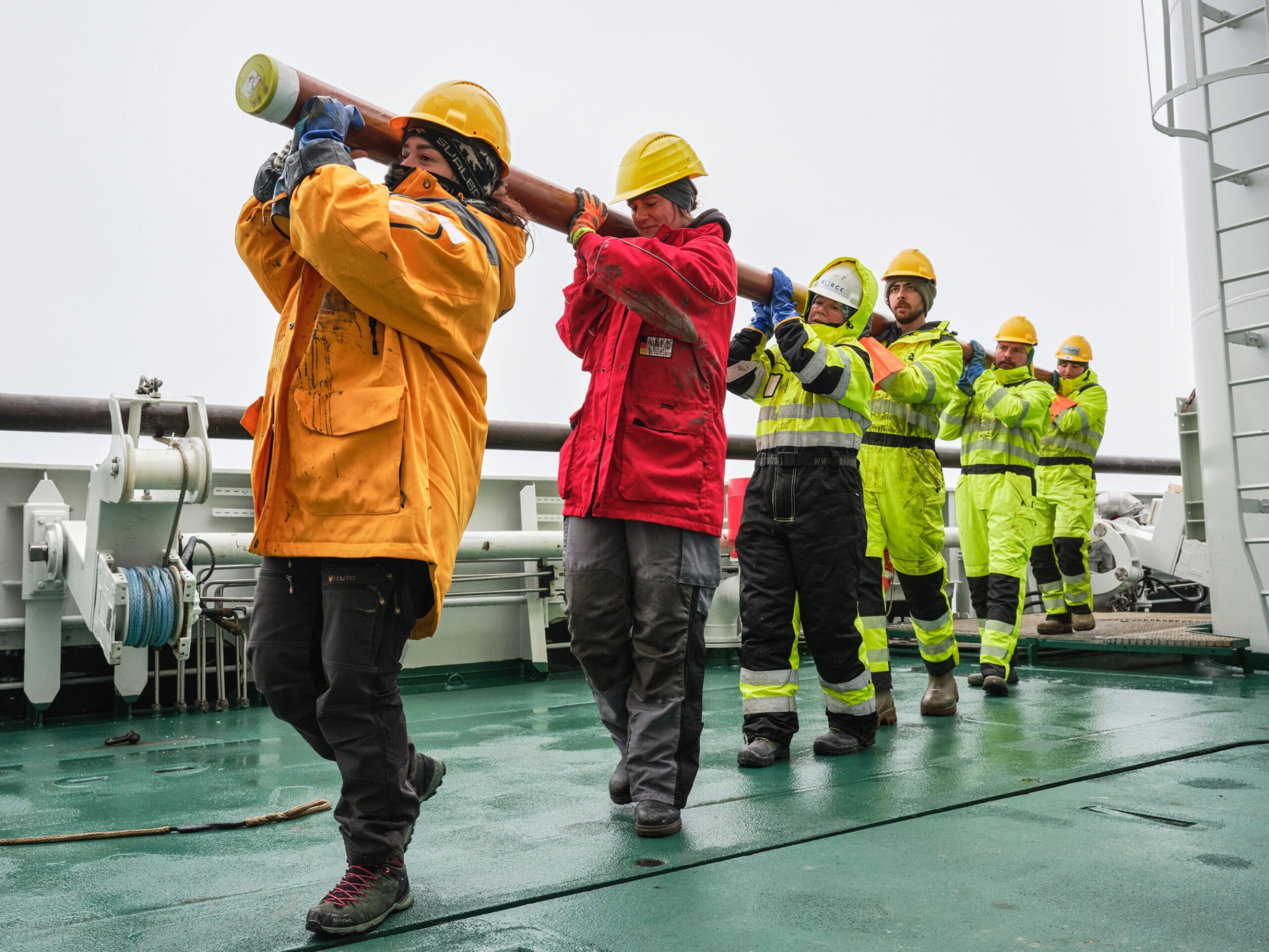 the crew in a line with the long pipe hoisted over their shoulder