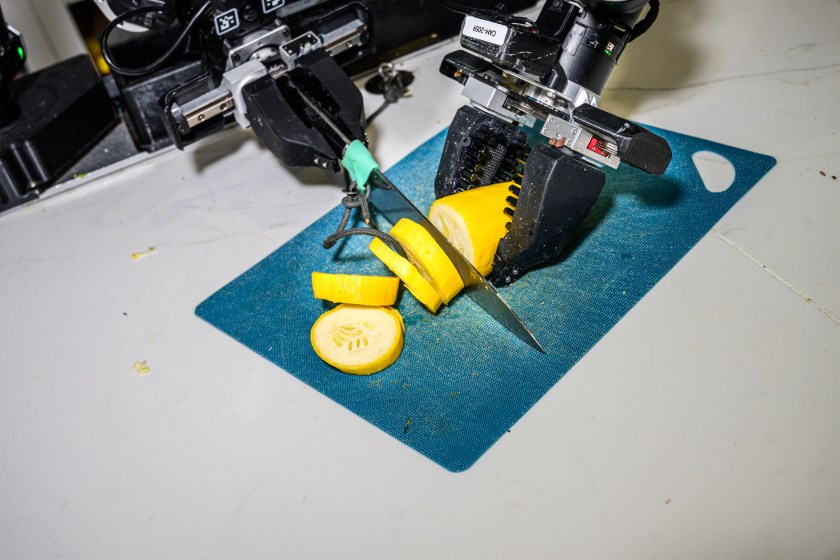 Robot grippers cutting a yellow squash with a kitchen knife